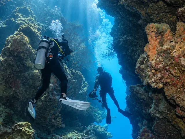 Two divers inside a sunlit crevice in the reef wall