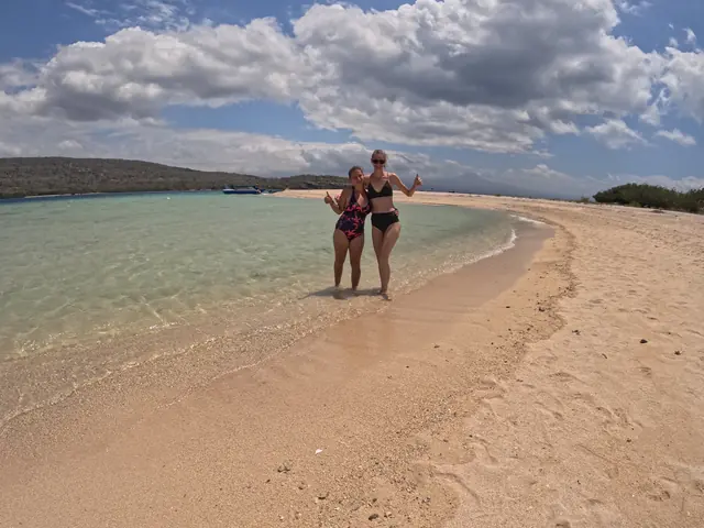 Two guests standing on a white-sand spit in turquoise water